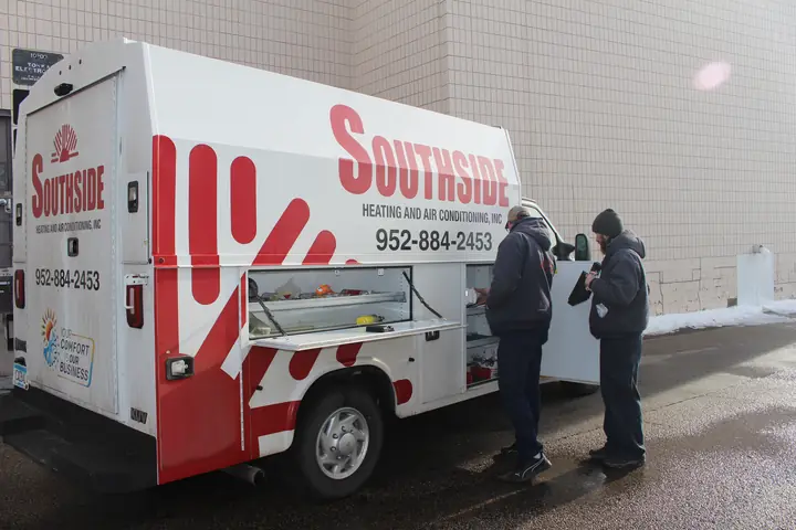 Two Southside Heating & Air Conditioning technicians at the open service body of a company truck
