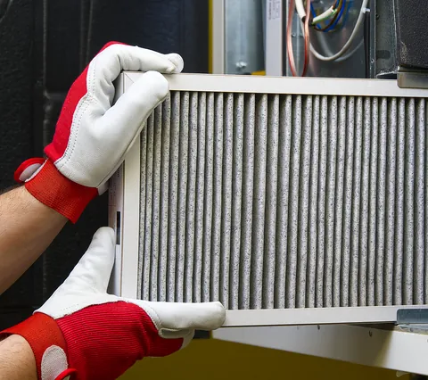 A technician in work gloves sliding a clean pleated filter into a home HVAC system